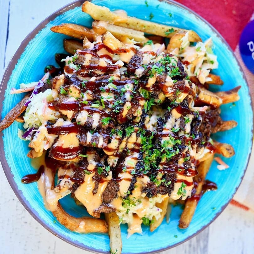 Close-up of loaded fries with meat, coleslaw, and sauces in a blue bowl.